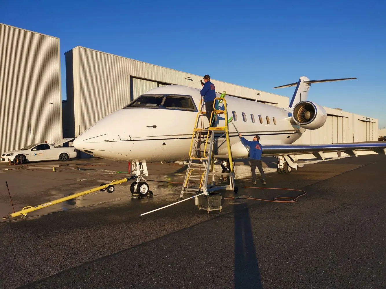 Detailing crew washing a Challenger business jet from a platform ladder